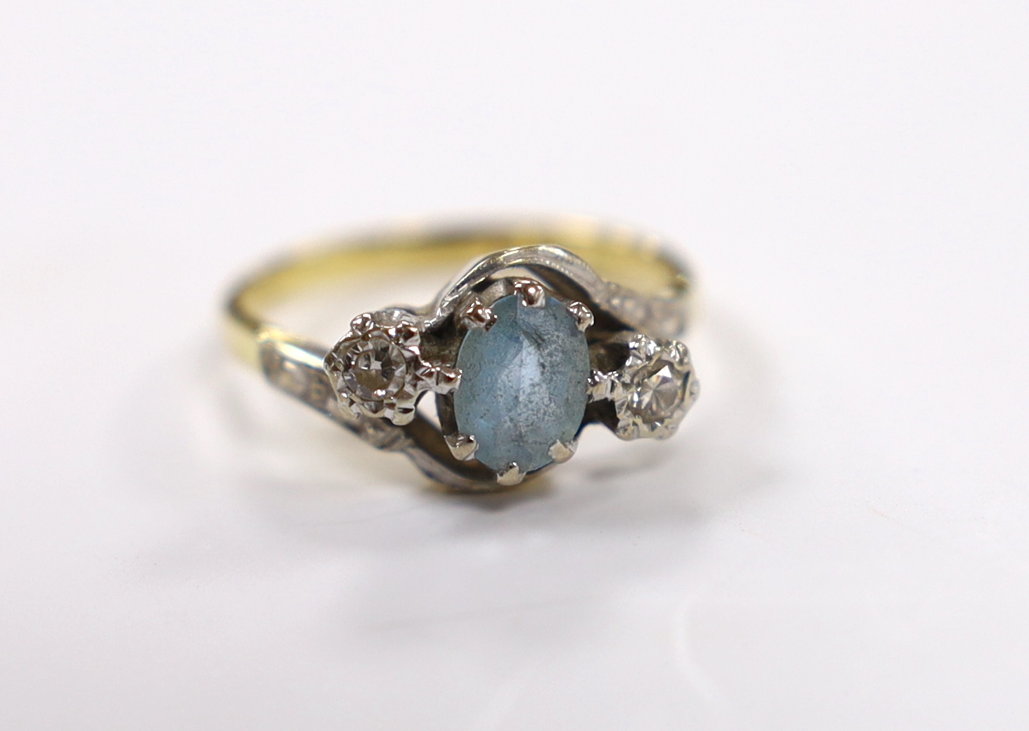 A modern 18ct gold, aquamarine and illusion set diamond three stone crossover ring, size N, gross weight 4.2 grams.